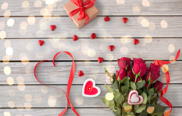 valentines day and holidays concept - close up of red roses, gift, red heart shaped chocolate candies and burning candle