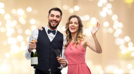 celebration and people concept - happy couple with bottle of champagne and glasses over beige background with festive lights