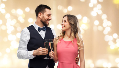 celebration and people concept - happy couple with champagne glasses toasting over beige background and festive lights