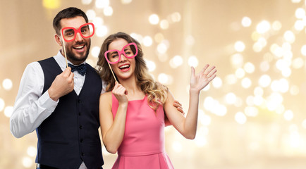 photo booth, fun and people concept - happy couple posing with party props over festive lights...