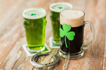 st patricks day, holidays and celebration concept - shamrock on glasses of beer and horseshoe on wooden table