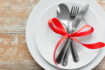 valentines day, table setting and festive dinner concept - plate with spoon, knife and fork tied...