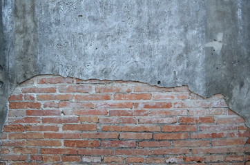 An aged, cracked and chipped stucco wall with an area of exposed brown brick. Brick wall background texture.