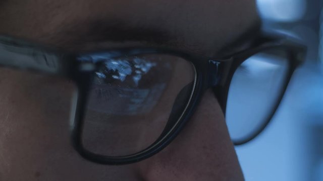 closeup of young man geek programmer in glasses working late at office, closeup eyes of male hacker working in data center