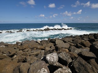 Gorgeous waves slapping against the rocks on a sunny day at a tropical island, with more rocks in the foreground 