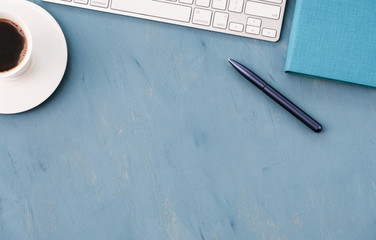 A keyboard, a blue pen and a notebook on a blue desk top.