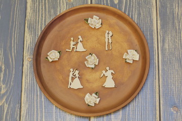 Obraz na płótnie Canvas Romantic composition of vintage figures of dancing lovers and satin decorative flowers in pastel colors on clay dish for day of lovers. Dark wooden background.
