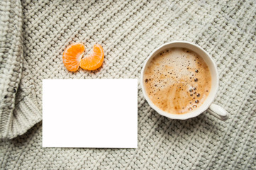 Obraz na płótnie Canvas A cup of cooffee on knitted beige background with tangerine and copyspace. Flat lay style.