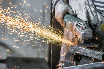 Working man with angle grinder, process of cutting carbonated steel metal with quantity of sparks in workshop