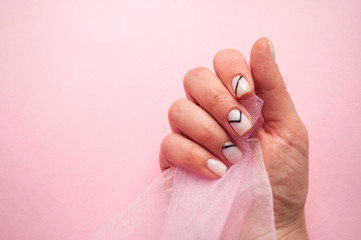 Young woman's hand with beautiful manicure on pink background holding a piece of tulle with copyspace.