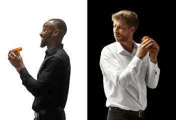 Men eating a hamburger and donut on a black and white background. The happy afro and caucasian men....