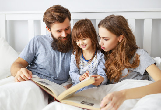 happy family mother, father and child read a book, a fairy tale  in bed