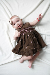 Cute adorable baby girl lying alone dressed on a white bed.Little child looking at the camera . Baby fashion clothes.A child of 5 months is having fun alone,lying on a snow-white bed.