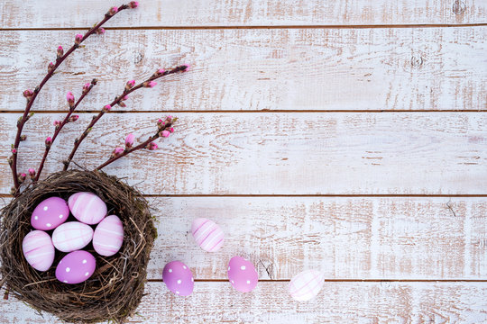 Easter background with colorful eggs in a nest over white wooden rustic table - copy space