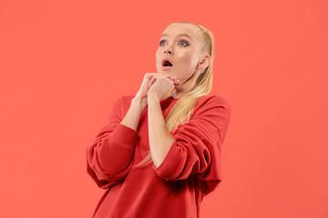 Wow. Beautiful female half-length front portrait isolated on coral studio backgroud. Young emotional surprised woman standing with open mouth. Human emotions, facial expression concept. Trendy colors