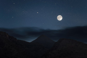 Silhouette of mountains on the huge full moon and night sky background.
