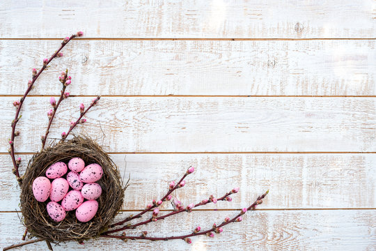 Easter background with colorful eggs in a nest over white wooden rustic table - copy space