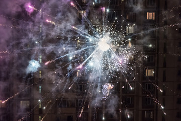 Colorful closeup fireworks light up on the windows of a residential building background.