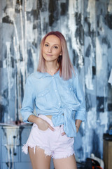 Naklejka premium Attractive young charming woman posing on a gray-blue background in summer clothes. Sexy young female female student posing in studio in denim clothes