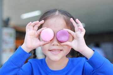 Happy little Asian child girl playing and holding Macaroons on her eyes.