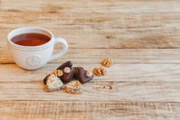 Obraz na płótnie Canvas Cup of hot black tea with chocolate candy and walnuts on wooden table, selective focus.