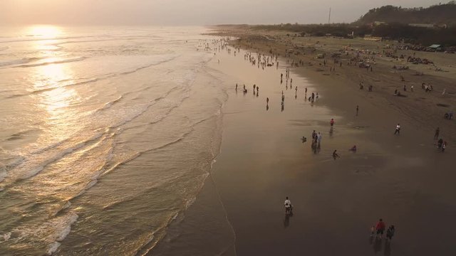 sandy beach parangtritis near ocean with big waves, people in tropical resort at sunset. Yogyakarta, Indonesia. aerial view seascape, ocean and beautiful beach. Travel concept. Indonesia, java