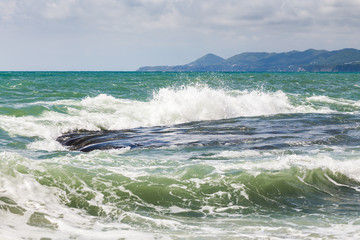 Waves in turquoise sea crashes over  rocky coast at warm sunny day.  Tuapse, Russia