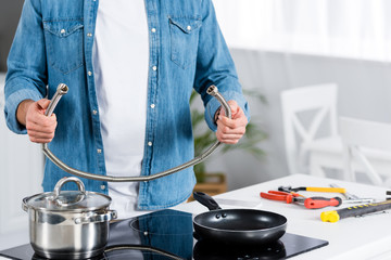 cropped view of man holding metal hose in hands at kitchen