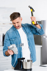 aggressive adult man screaming while holding mixer and hammer