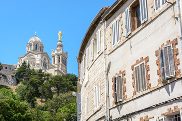 Fototapeta na wymiar Rear view of Notre-Dame de la Garde basilica on top of the hill in Marseille, France, seen from the street below with old townhouses in the foreground.