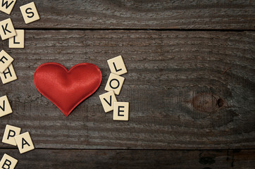 Red fabric heart on wooden table along with the word love