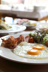 Breakfast set with fried eggs, bacon, sausages, beans, toasts, fresh salad and fruit on wood table