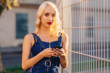 emotive blond attractive girl in sunglasses with phone in summer sunshine urban