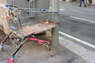 Abandoned shopping cart of a homeless chained to lamppost with padlock. Painted in pink.