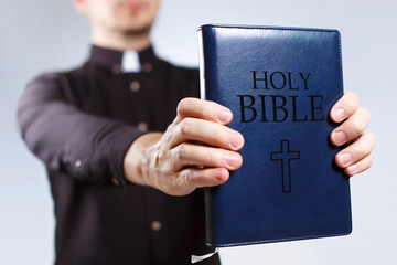 Young priest holding the Holy Bible on neutral background