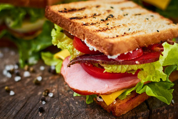 Homemade sandwich with ham, lettuce, cheese and tomato on a wooden background