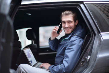 handsome businessman sitting in luxury limousine, working on laptop computer