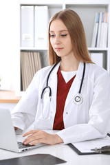 Close-up of unknown female doctor typing on laptop computer while sitting  at the table