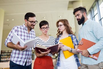 Happy young university students studying with books in library