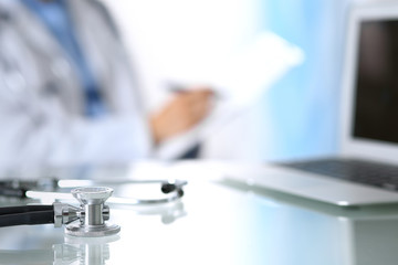 Stethoscope lying on glass desk with laptop computer at busy physician background. Medicine or pharmacy concept. Medical tools at doctor working table