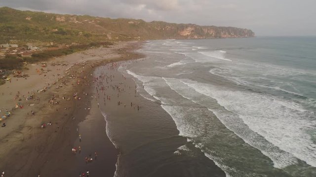 sandy beach parangtritis near ocean with big waves, people in tropical resort at sunset. Yogyakarta, Indonesia. aerial view seascape, ocean and beautiful beach. Travel concept. Indonesia, java