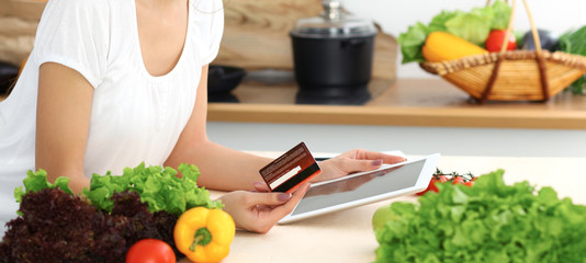 Beautiful Hispanic  woman cooking while using tablet computer in kitchen or  making online shopping by touchpad and credit card. Housewife found new recipe for dinner