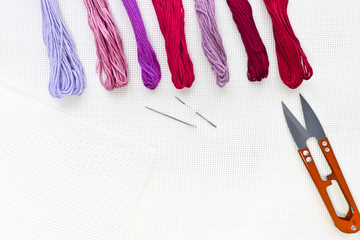 Flat lay top view with an embroidery canvas, needles, threads in red colours