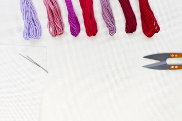 Flat lay top view with an embroidery canvas, needles, threads in red colours