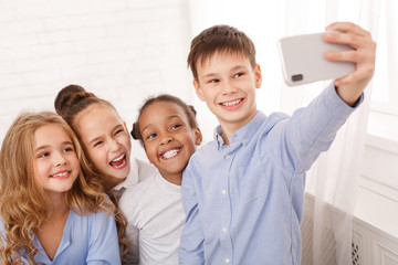 Happy schoolchildren taking selfie in light classroom