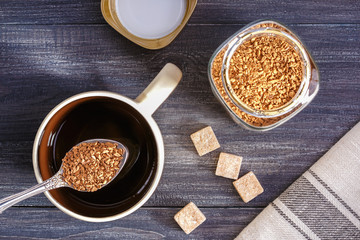 Instant coffee. Cup with hot water and instant coffee spoon on wooden table. Top view.