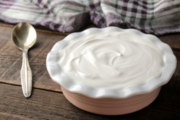 greek yogurt in a ceramic bowl next to a spoon on a brown wooden background