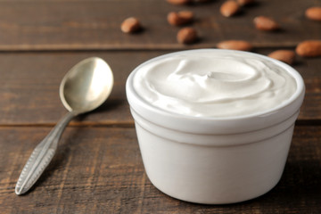 Greek yogurt in a ceramic bowl and with almond nut next to a spoon on a brown wooden background.