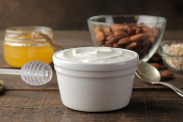 Greek yogurt in a ceramic bowl with almonds and honey next to a spoon on a brown wooden background. healthy food. natural yoghurt. breakfast.