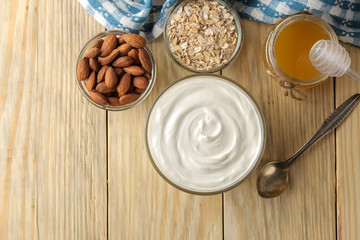 Greek yogurt in a glass bowl next to oatmeal and honey and almond nut on a natural wood background. healthy food. natural yoghurt. breakfast. top view